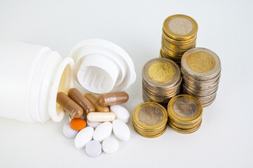 Medicines and tablets, coming out of a container, with stacks of coins next to them. Cost of medicines and price increase. 
