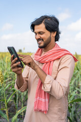 vertical shot of farmer busy using mobile phone at agricultural farm land - concept of technology,...