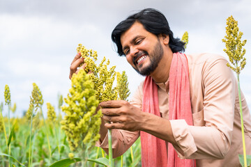 Happy smiling young farmer checking crop growth at farmland - concept of successful agriculture,...