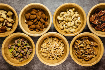 Different types of dried fruits in wooden bowls. Peanuts, cashews, almonds, pistachios, walnuts, pecans and brazil nuts. Top view.