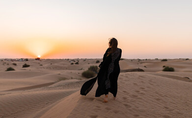 Back view of Beautiful mysterious woman in traditional arabic black long dress stands in the desert...