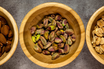Wooden bowl with roasted pistachios on a slate table. Top view, series photo with other dried fruits.