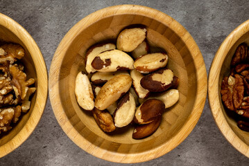 Wooden bowl with roasted brazil nuts on a slate table. Top view, series photo with other dried fruits.