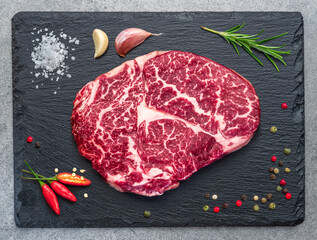 Raw ribeye steak on stone black serving plate. Flat lay.