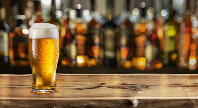 Glass of chilled beer on table and blurred sparkling bar background.