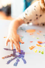A little girl painting with her hands on a white sheet of paper.