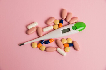 Pills and a thermometer on a pink background. The concept of an increase in the incidence of covid-19