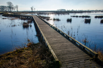 Wooden walkbridge for pedestrians across a shallow lake, partly coverd with ice near Dwingelo, The...