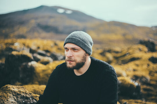 Portrait of young handsome man sitting on the nature and dreaming. Brutal male with a beard on lava fields in Iceland.