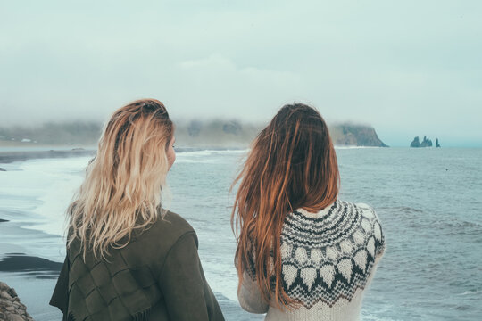 Back view of two woman standing on the shore of the sea and enjoying the landscape of black beach, troll toes in Iceland