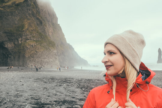 Portrait of young beautiful woman standing near the troll toes on the beach in Iceland and looking sideways.