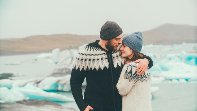 Tenderness portrait of young couple in lopapeysa sweaters standing in ice lagoon and enjoying the romantic date.