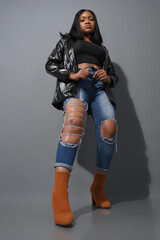 Full body shot of millennial girl in stylish outfit brown boots poses in looks at camera has serious expression leans behind and hands on her jeans. Female teenager 