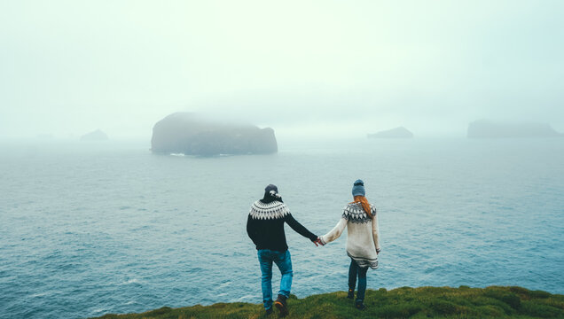 Back view of young couple standing on the edge of the cliff and looking on the sea, waves on the horizon in foggy day.