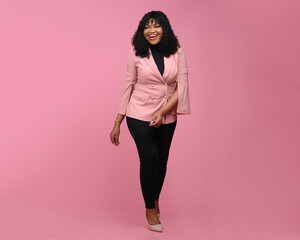 Full length view of confident cheerful african american businesswoman walking over a Pink background