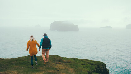 Back view of young traveling couple walking on the shore of the sea in foggy day together, resting on nature.