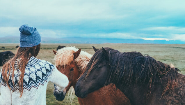 Young traveling woman standing near beautiful horse in Iceland mountains and touching the mane. Tourist female pats pony