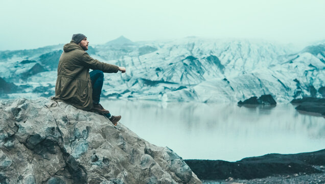 Young man sitting alone on the rock and enjoying the beautiful landscape of ice lagoon with lake in Iceland.