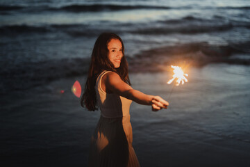 Smiling woman with sparkler on seashore