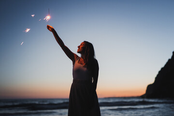 Smiling woman with sparkler on seashore