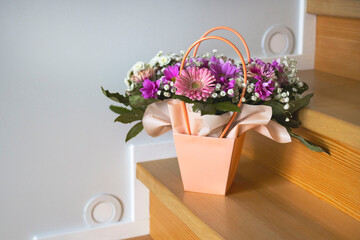 A composition of flowers in a festive box stands on the stairs with lighting. A gift for a beloved woman