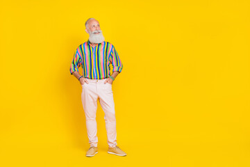 Photo of satisfied retired man with white beard dressed striped shirt white trousers look empty space isolated on yellow color background