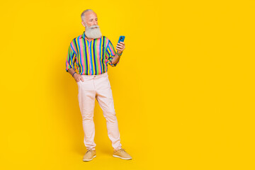 Fototapeta premium Full size portrait of confident serious aged man hold use telephone empty space isolated on yellow color background