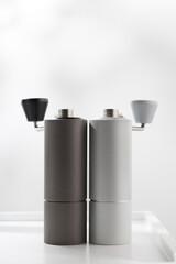 Vertical photo of light gray manual coffee grinder and dark gray on white table.