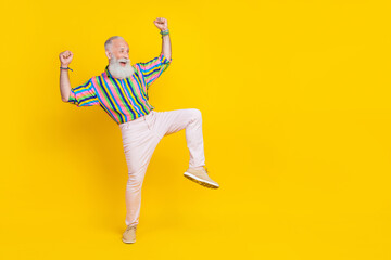 Fototapeta na wymiar Full length photo of positive funky guy dressed striped shirt looking empty space rising fists isolated yellow color background