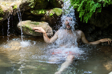 young man lying under a waterfall cooling himself off
