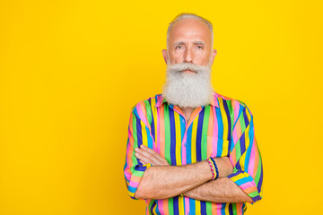 Photo of handsome serious retired man with white beard dressed striped shirt standing arms crossed isolated on yellow color background