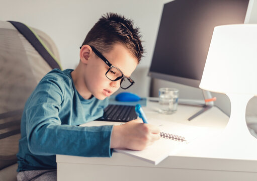 Boy sits at desk in the living room with computer doing homework during the day. Shot of a determined young boy doing his homework at home