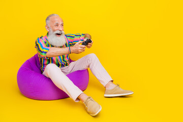 Full length photo of pretty impressed guy dressed striped shirt enjoying playstation empty space isolated yellow color background