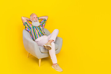 Full length photo of cheerful positive man sit chair arms behind head look empty space isolated on yellow color background