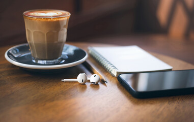 Heart shape of latte coffee in old style glass and mobile phone, note book, wireless headphones on...