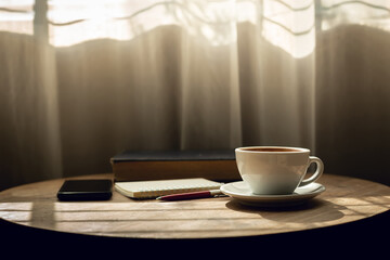 Close up view, white coffee cup with old book and smart phone on wooden table near the window and the sun is shining through, vintage color tone