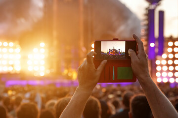 Hand with a smartphone record live music festival and taking photos of the concert.