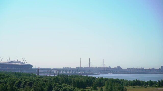 Urban landscape. View of the river, blue water, embankment. Modern cable-stayed highway bridge. Stadium building and summer park. Saint-Petersburg, Russia. Zenith arena and zsd.