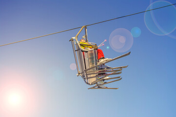 Skiers in ski lift, adult and kid going uphill in a ski resort at blue and yellow clean gradient sky at sunset warm light with lens flare and direct sunlight.