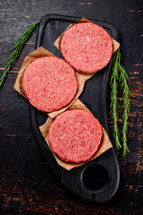 Raw burger on a cutting board with rosemary.