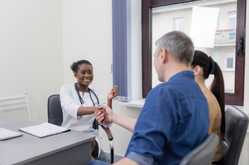 Obraz premium a happy married couple thanks the doctor by shaking his hand. Consultation with a family doctor, positive health news