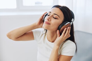 Fototapeta premium Woman listening to music on headphones sitting at home on a chair with her eyes closed, a smile and a good mood, a meditation to relieve stress