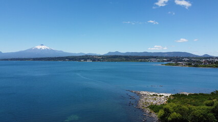 Aerial view of the volcano and mountains, on the shore of a lake in summer, with the city in the distance.