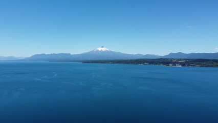 Aerial view of the volcano and mountains, on the shore of a lake in summer, with the city in the distance.