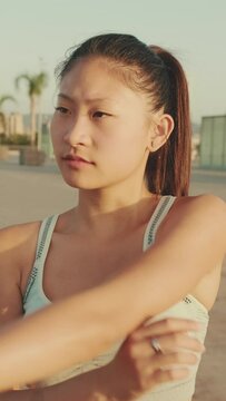 VERTICAL VIDEO: Asian girl in sports top does workout, stretching and gymnastics at morning time on modern buildings background