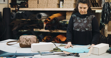 Seamstress at work. Dressmaker making clothes and bags in workshop. Tailor marking fabric. Woman working at table with cut textile, thread, pins, needles, cutouts. Upcycling concept. Banner copy space