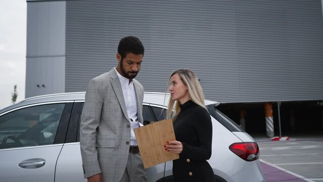 Young woman selling electric car to multiracial businessman.