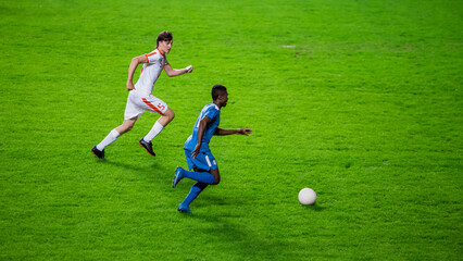 Professional Soccer Football Match Championship: Blue Team Players Attacks, White Player Tries to Tackle. Action Game on International Tournament. Sport Broadcast Television Channel Concept.