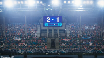 Football Soccer Stadium Championship Match, Scoreboard Screen Showing Score of 2:1. Crowd of Fans Cheering, Screaming, Having Fun. Sport Channel Television Advertising Concept. Wide Shot.