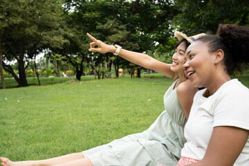 Naklejka premium Young attractive Asian buddy woman sitting in a park, togetherness. Outdoor activity in summer to relax outside with friend,relationship.